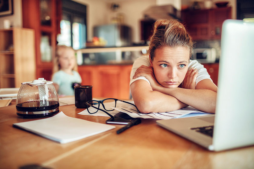 worried mom working on computer with child in background