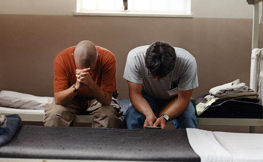 two men pray together in a prison cell